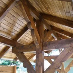 Drewniana konstrukcja dachu z belek i desek, impregnowana na ciemny brąz, widok od dołu, detale zdobione frezami.