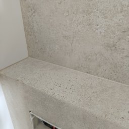 Grzegorz Ostrowski - Fragment ściany i półki wykończonej płytkami imitującymi kamień w łazience, widoczny otwór na instalację.