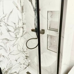 Grzegorz Ostrowski - Kabina prysznicowa z czarną ramą, marmurowymi płytkami z motywem kwiatowym na ścianie, wbudowane półki w ścianie