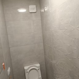 Grzegorz Ostrowski - Jasna łazienka po remoncie z toaletą, umywalką i grzejnikiem, wykończona płytkami w dwóch wzorach: gładkimi i z trójwymiarową fakturą.