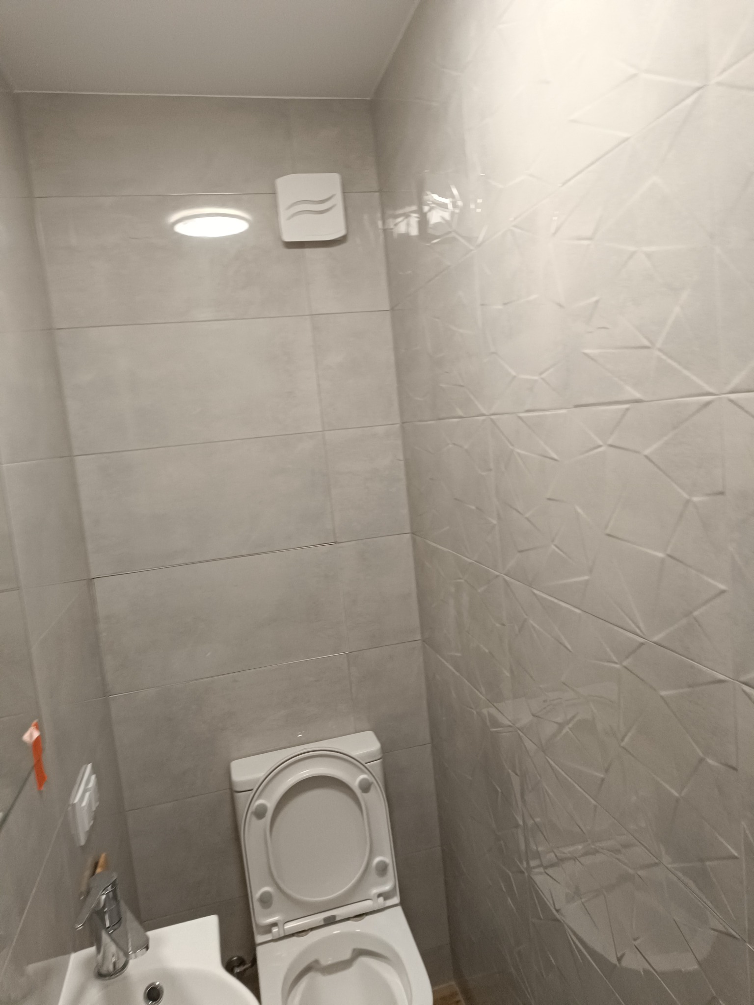 Jasna łazienka po remoncie z toaletą, umywalką i grzejnikiem, wykończona płytkami w dwóch wzorach: gładkimi i z trójwymiarową fakturą.