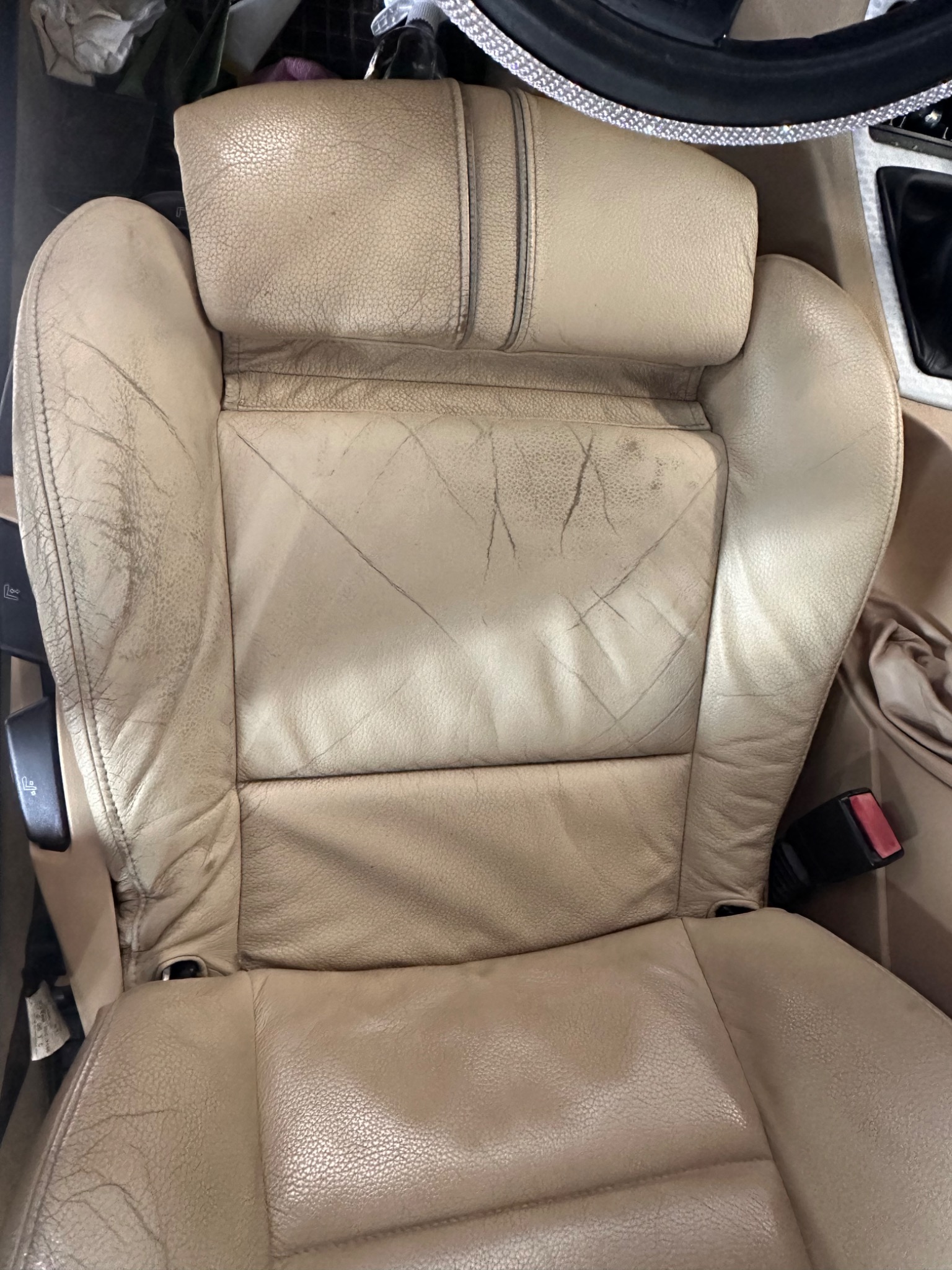 Beżowe skórzane siedzenie samochodowe z widocznymi śladami użytkowania, pęknięciami i zabrudzeniami na powierzchni skóry.