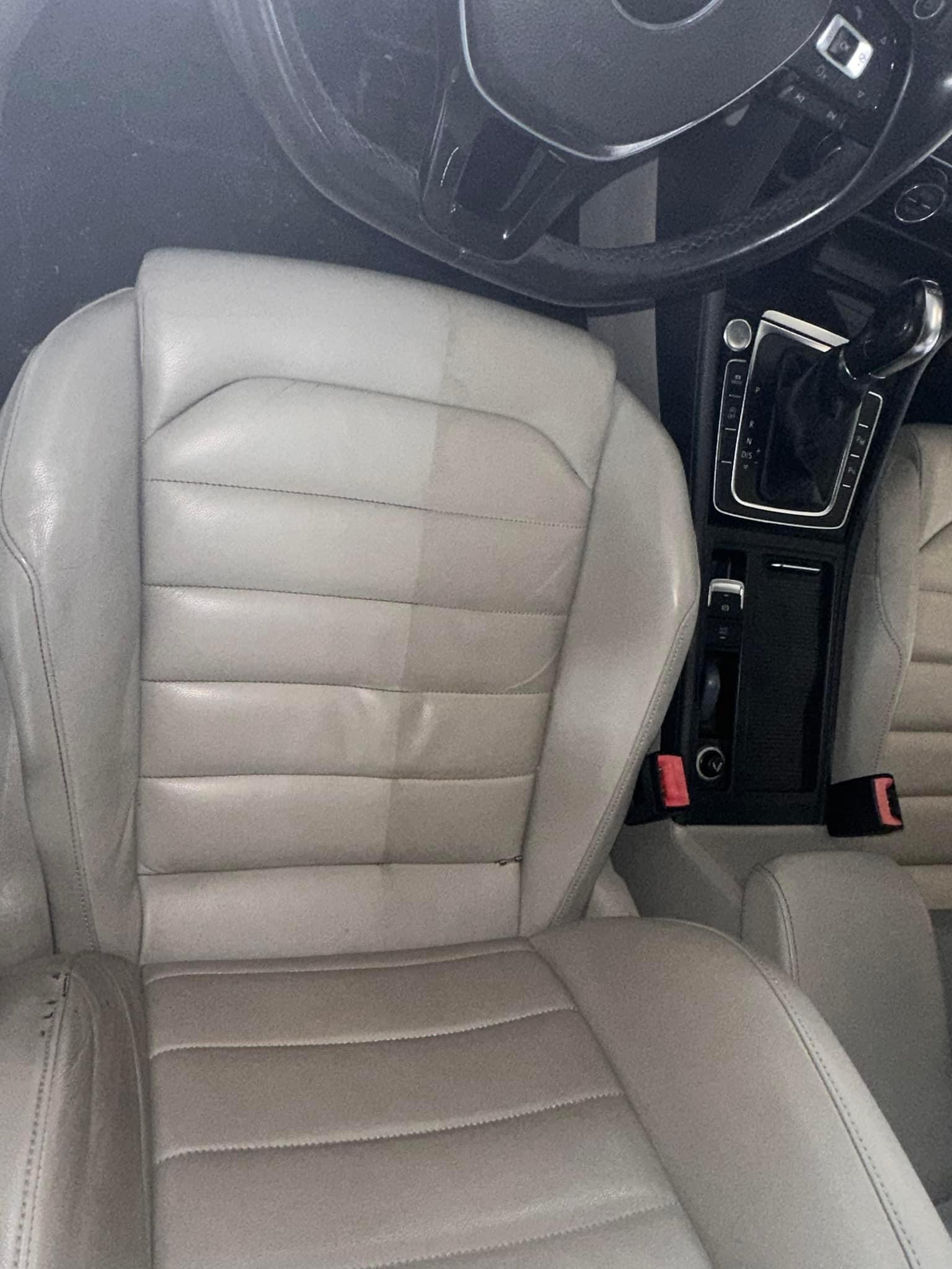 Skórzane siedzenie samochodowe w odcieniach szarości, widoczna różnica w czystości między wypraną a niewypraną częścią, wnętrze pojazdu z kierownicą i konsolą środkową w tle.