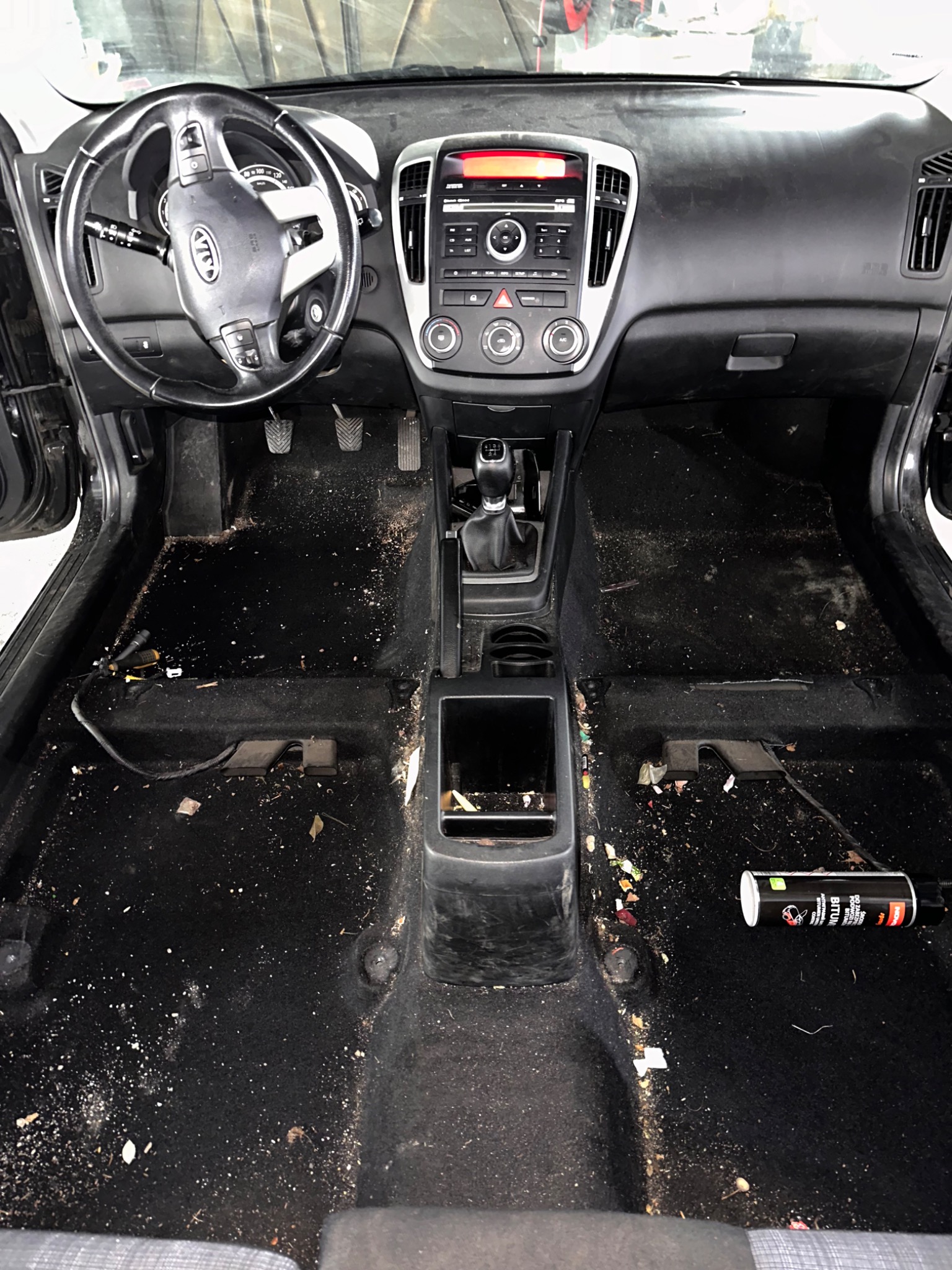 Wnętrze samochodu w Piotrków Trybunalski przed czyszczeniem: bardzo zabrudzona, czarna tapicerka podłogowa, widoczne okruchy, piasek i śmieci, a także puszka preparatu do czyszczenia.