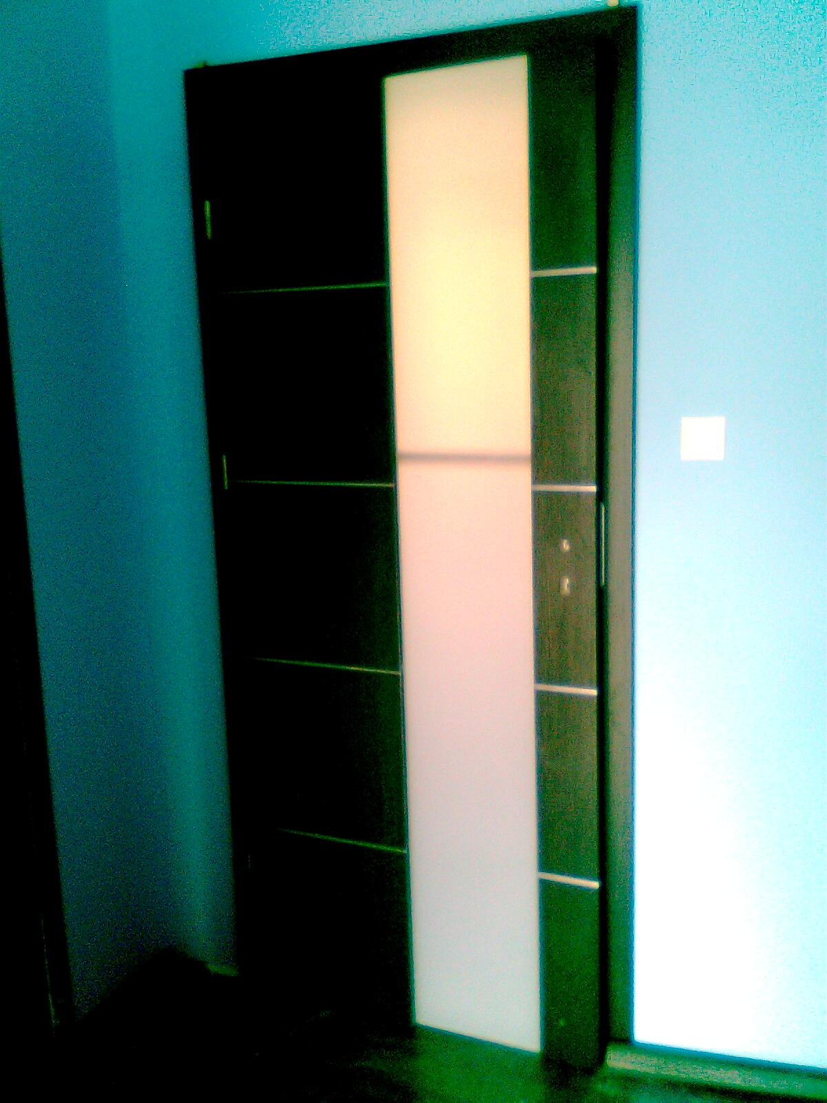 Nowoczesne, ciemne drzwi wewnętrzne z długim, pionowym, mlecznym szkłem, zamontowane w pokoju z niebieskimi ścianami.