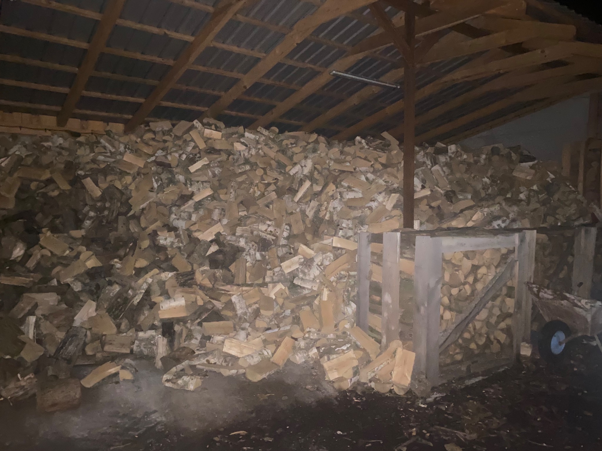 Stos drewna kominkowego pod zadaszeniem w Grabówce, widoczny fragment wózka transportowego.