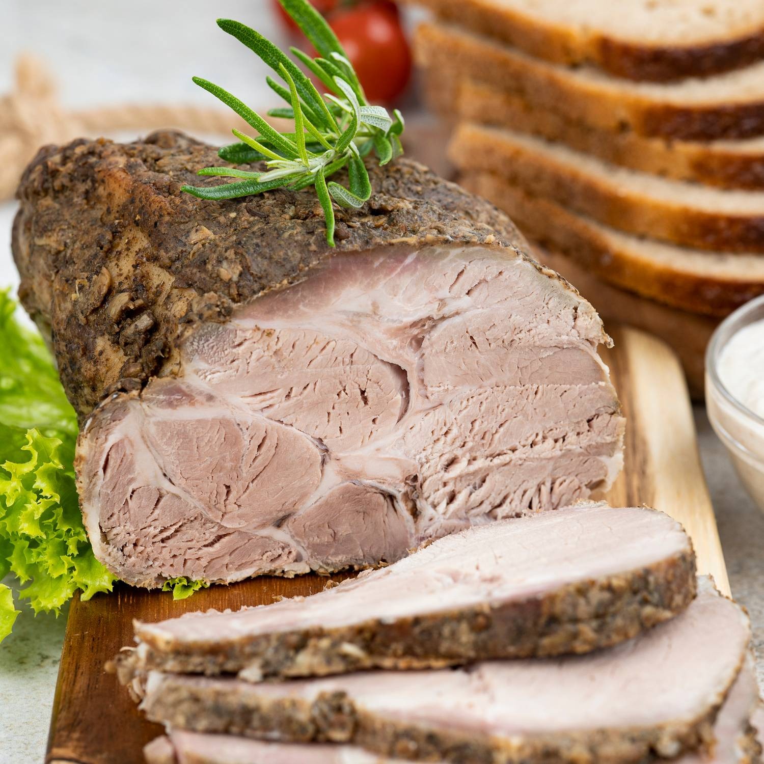 Pieczony schab wieprzowy, udekorowany gałązką rozmarynu, podany na drewnianej desce z kromkami chleba razowego i sosem.