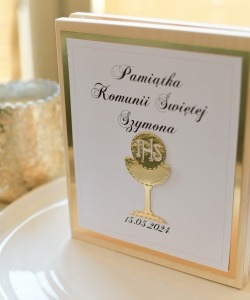 Pamiątka Pierwszej Komunii Świętej Szymona w drewnianej ramce z kielichem IHS i datą 15.05.2024, ustawiona na białym talerzu obok świecznika.