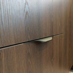 Blenda Studio meble na wymiar - Szczegółowe ujęcie frontu szuflady z drewnopodobną okleiną i minimalistycznym, metalowym uchwytem wpuszczanym, podkreślające fakturę i nowoczesne wykończenie.