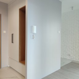 Blenda Studio meble na wymiar - Nowoczesna szafa wnękowa z drewnianymi akcentami i minimalistycznymi uchwytami, wkomponowana w jasne wnętrze z białą cegłą i marmurową podłogą.