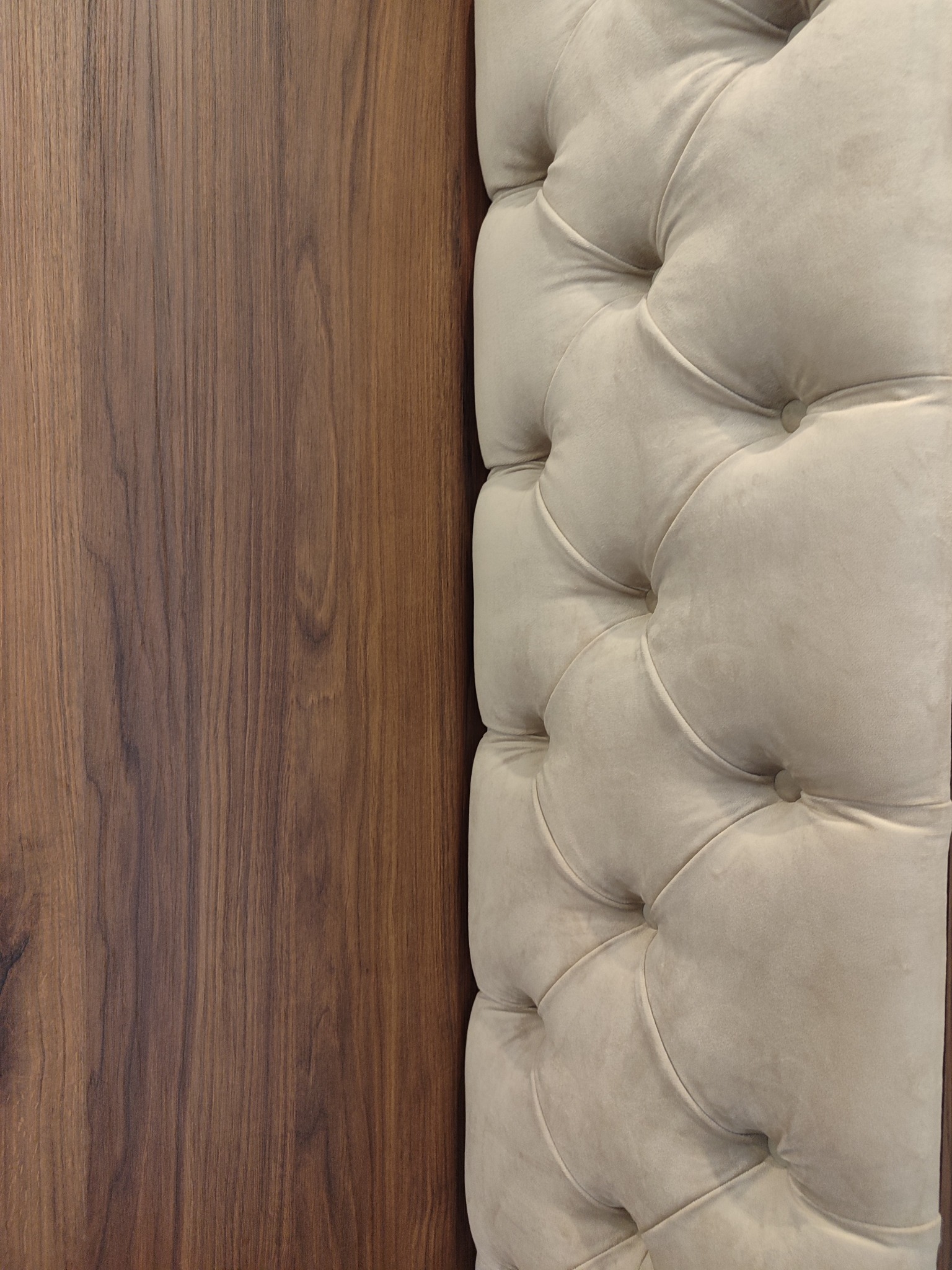 Fragment wezgłowia łóżka z beżową tapicerką w romby, sąsiadującego z panelem z ciemnego drewna o wyraźnym usłojeniu. Detal wykończenia wnętrza.