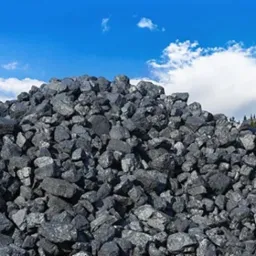 G&oacute;ra czarnego węgla kamiennego na tle błękitnego nieba z białymi chmurami i zielonym lasem iglastym w oddali.