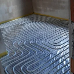 Białe rurki ogrzewania podłogowego ułożone na czarnej siatce w pomieszczeniu w Toszku, przygotowane do zalania wylewką.