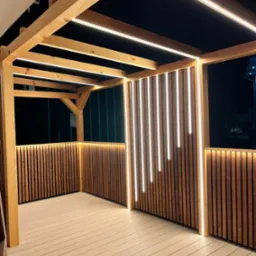 Drewniana altana z nowoczesnym oświetleniem LED, pionowe panele z lamelami i deski podłogowe w ciepłych odcieniach brązu, oświetlona od góry i z boków, nocne ujęcie.