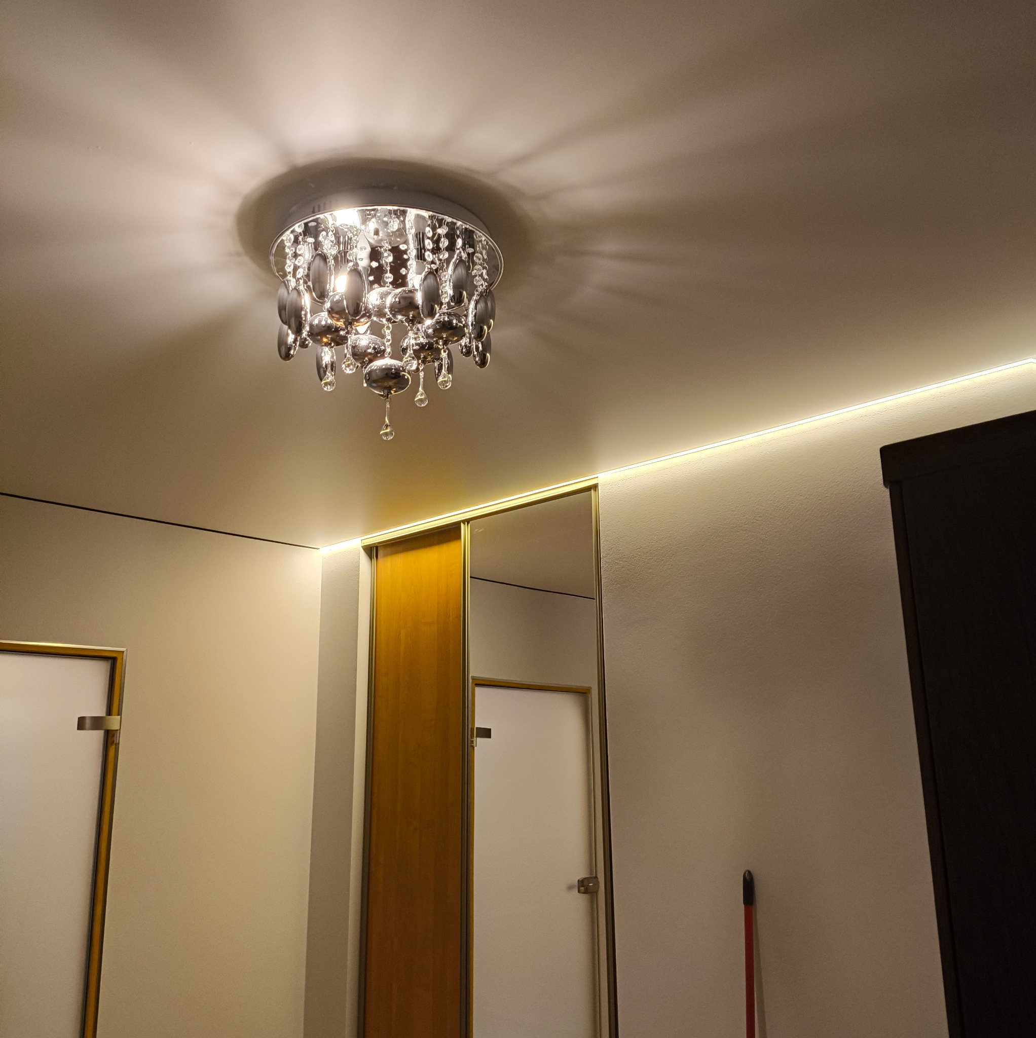 Pokój z oświetleniem LED na suficie, ozdobnym żyrandolem i zabudową z przesuwnymi drzwiami z lustrem. Nowoczesne wykończenie wnętrza.