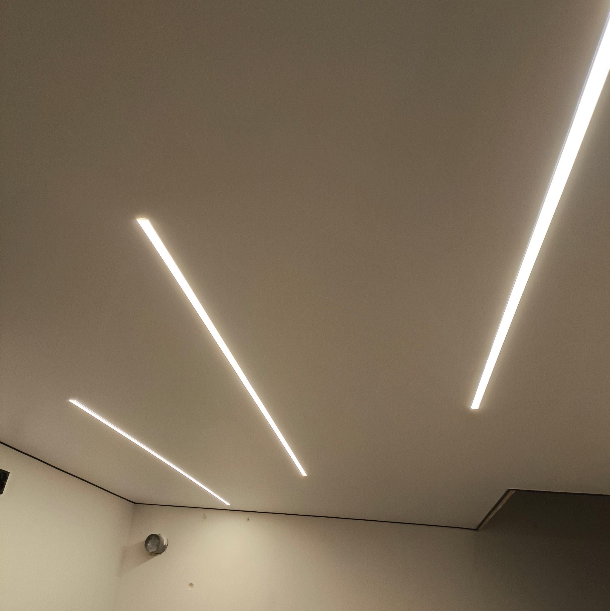 Jasne, liniowe oświetlenie LED wkomponowane w gładki, beżowy sufit. Minimalistyczny design z akcentem na nowoczesne wykończenie wnętrza.