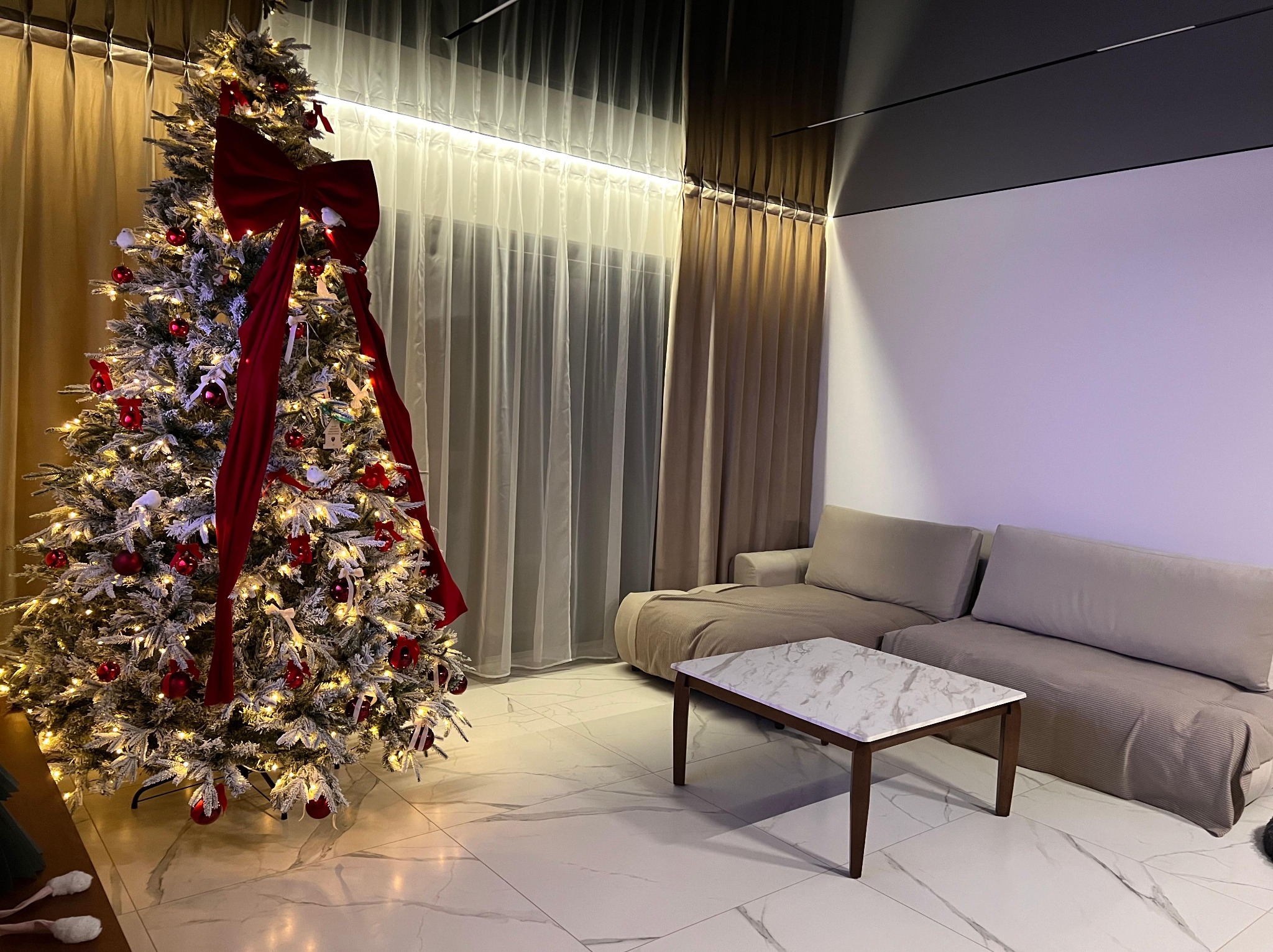 Nowoczesny salon z marmurową podłogą, sofą i choinką z czerwonymi ozdobami. Oświetlenie sufitowe podkreśla minimalistyczny design wnętrza.