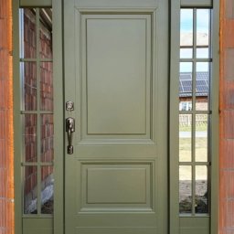 Piętro i Parter - Zewnętrzne drzwi wejściowe w odcieniach zieleni, z bocznymi przeszkleniami, zamontowane w surowym murze. Widoczne panele słoneczne w odbiciu szyby.