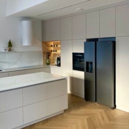 Piętro i Parter - Jasna kuchnia z wyspą i parkietem w jodełkę. Minimalistyczne szafki, nowoczesny okap cylindryczny i duża lodówka side-by-side. Dekoracje i oświetlenie punktowe.