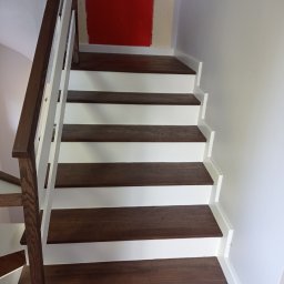 Usługi Parkieciarskie Bartłomiej Gadomski - Nowoczesne schody drewniane z ciemnymi stopniami i białymi podstopnicami, widoczne fragmenty pomalowanej na czerwono ściany w tle.