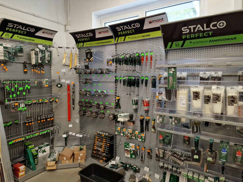 Ekspozycja narzędzi i akcesoriów budowlanych marki Stalco Perfect w sklepie, widoczne wiertła, śruby, poziomice, pędzle i inne artykuły na perforowanych ścianach z oświetleniem górnym.