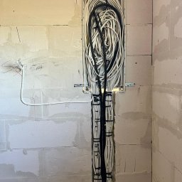 Joanna Magierska-usługi elektryczne - Pionowy kanał w ścianie z betonu komórkowego wypełniony wiązką białych i czarnych przewodów elektrycznych, zabezpieczonych czarnymi opaskami zaciskowymi.