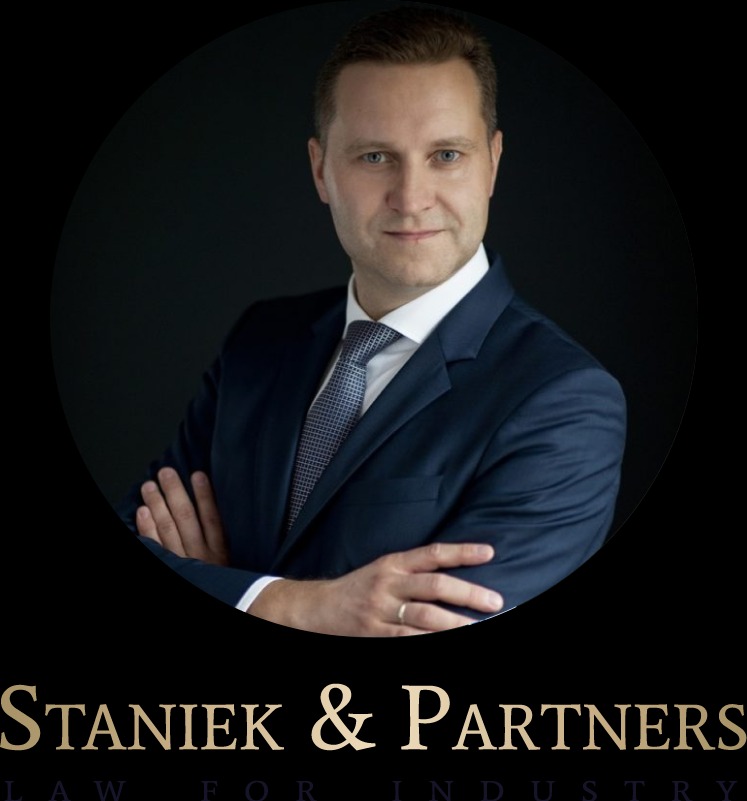 Portret mężczyzny w garniturze, z rękami skrzyżowanymi i widocznym pierścieniem, na ciemnym tle z logo firmy prawniczej Staniek & Partners.