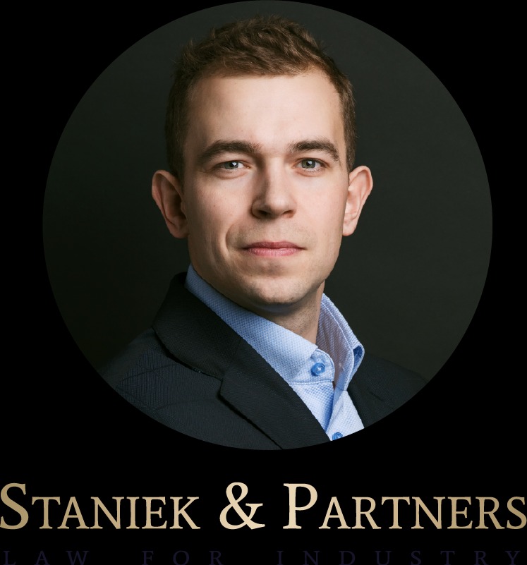 Portret młodego mężczyzny w garniturze i błękitnej koszuli na ciemnym tle, w okręgu. Poniżej nazwa firmy 'Staniek & Partners Law for Industry' w kolorze złotym.