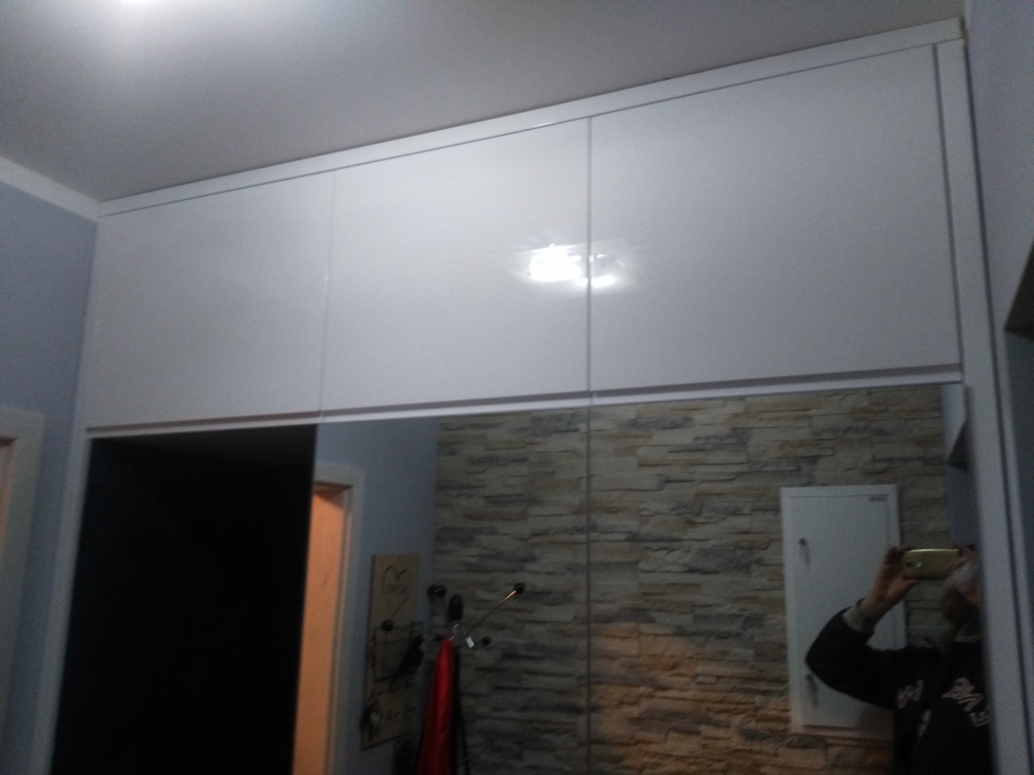 Białe szafki pod sufitem nad lustrem z odbiciem ściany z imitacją kamienia i wieszakiem na ubrania.