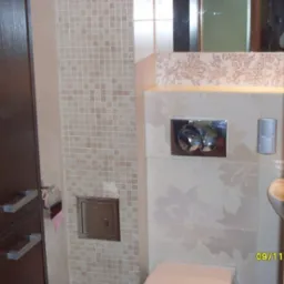 Wykończona łazienka w Łodzi: beżowe mozaiki i płytki z kwiatowym wzorem, zabudowa z ciemnego drewna, elementy armatury.