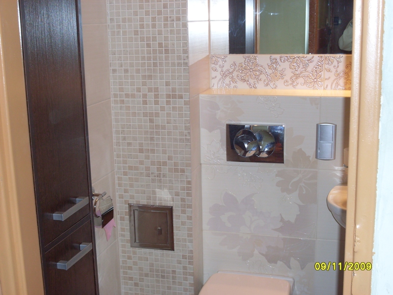 Wykończona łazienka w Łodzi: beżowe mozaiki i płytki z kwiatowym wzorem, zabudowa z ciemnego drewna, elementy armatury.