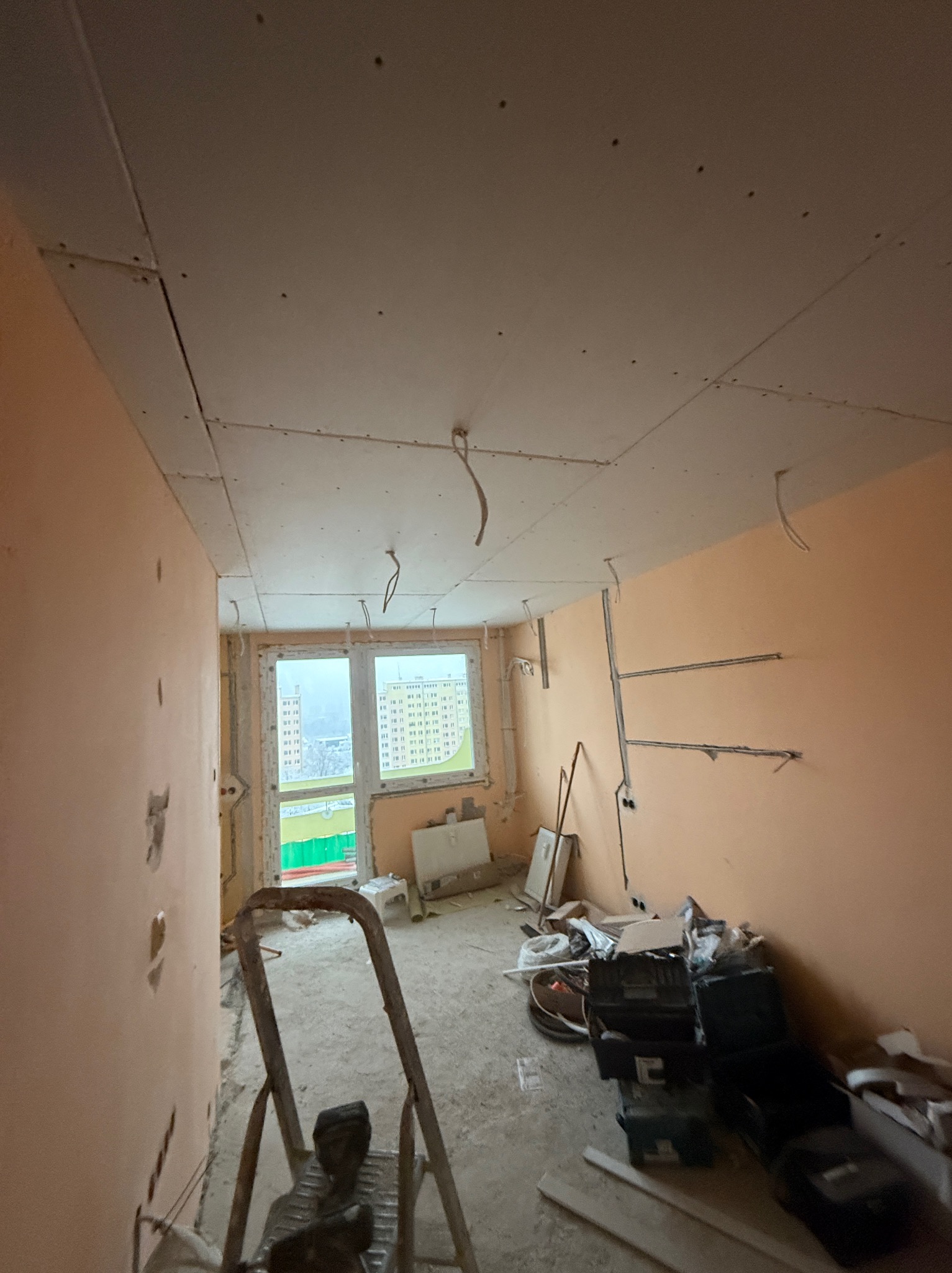 Montaż płyt gipsowych na suficie w Kamiennej Górze. Widoczne kable, ślady po szpachlowaniu na ścianach i drabina. Prace wykończeniowe w surowym stanie.