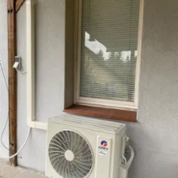 Zewnętrzna jednostka klimatyzacji marki Gree zamontowana na elewacji budynku w Białymstoku, widoczne rury odprowadzające skropliny i przewody elektryczne.