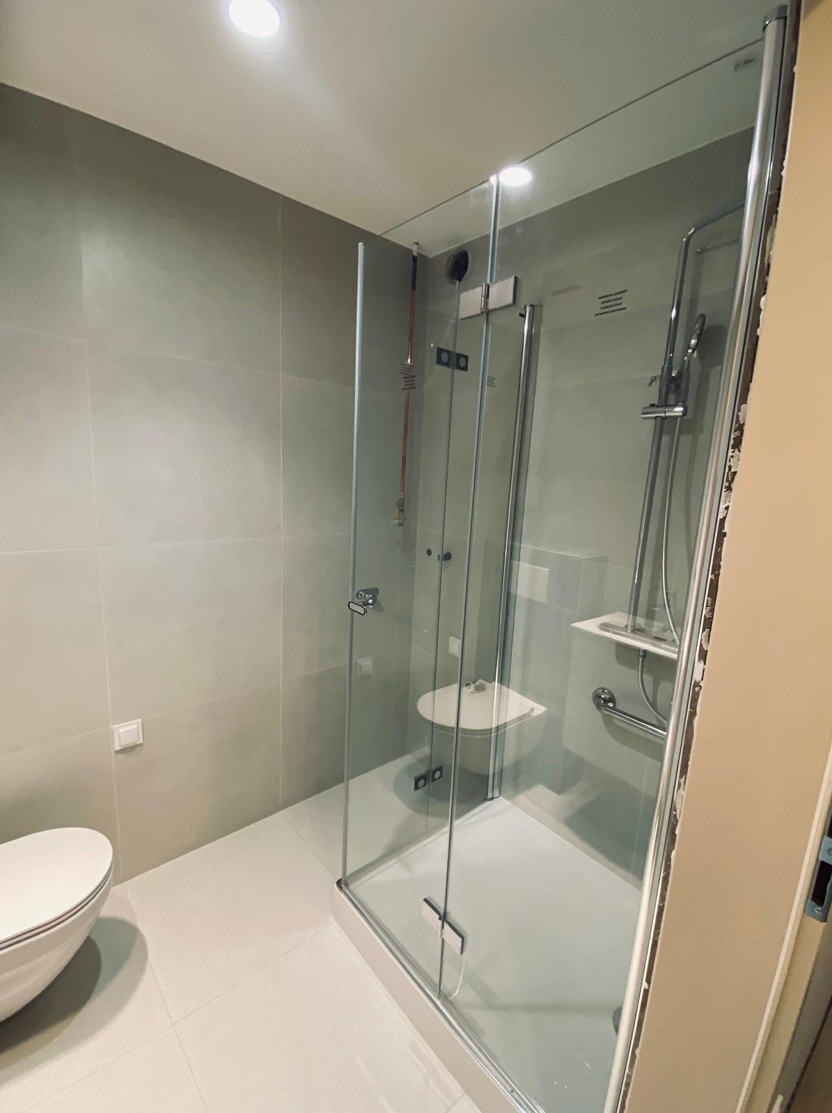 Nowoczesna kabina prysznicowa ze szklanymi drzwiami w łazience w Katowicach, widoczna toaleta i szare płytki na ścianach.