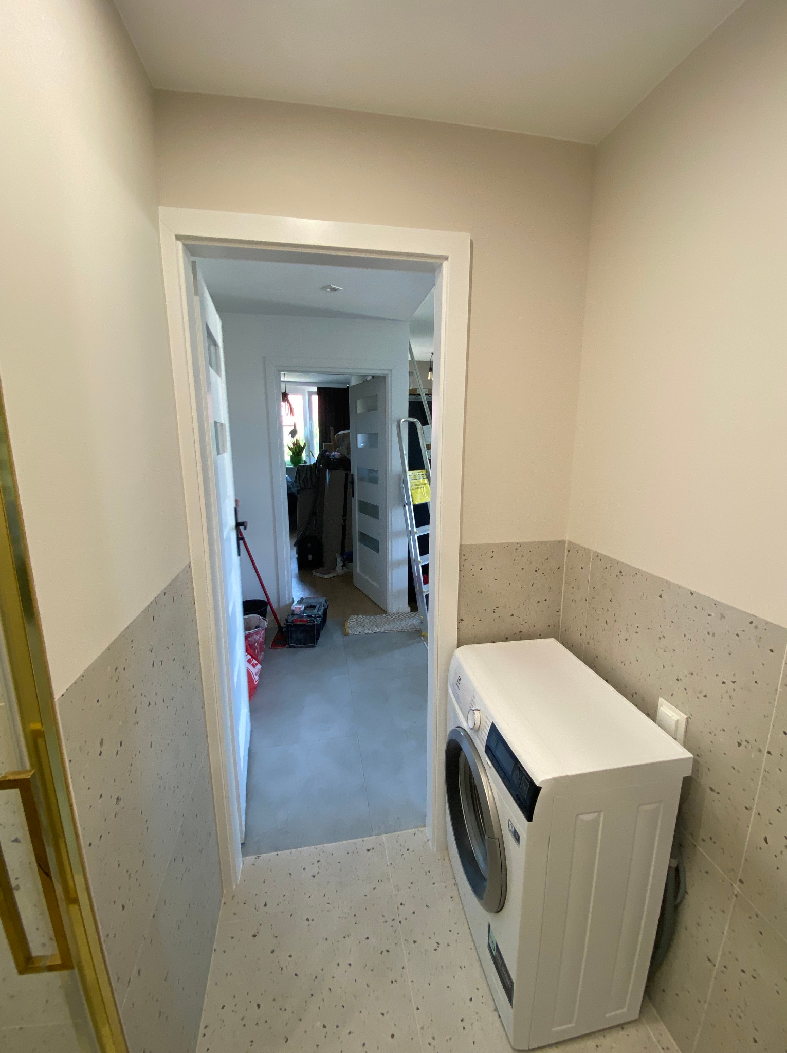 Wnętrze łazienki po remoncie z pralką, wykończone płytkami lastryko na ścianach do połowy wysokości, z widokiem na dalszą część mieszkania przez otwarte drzwi.