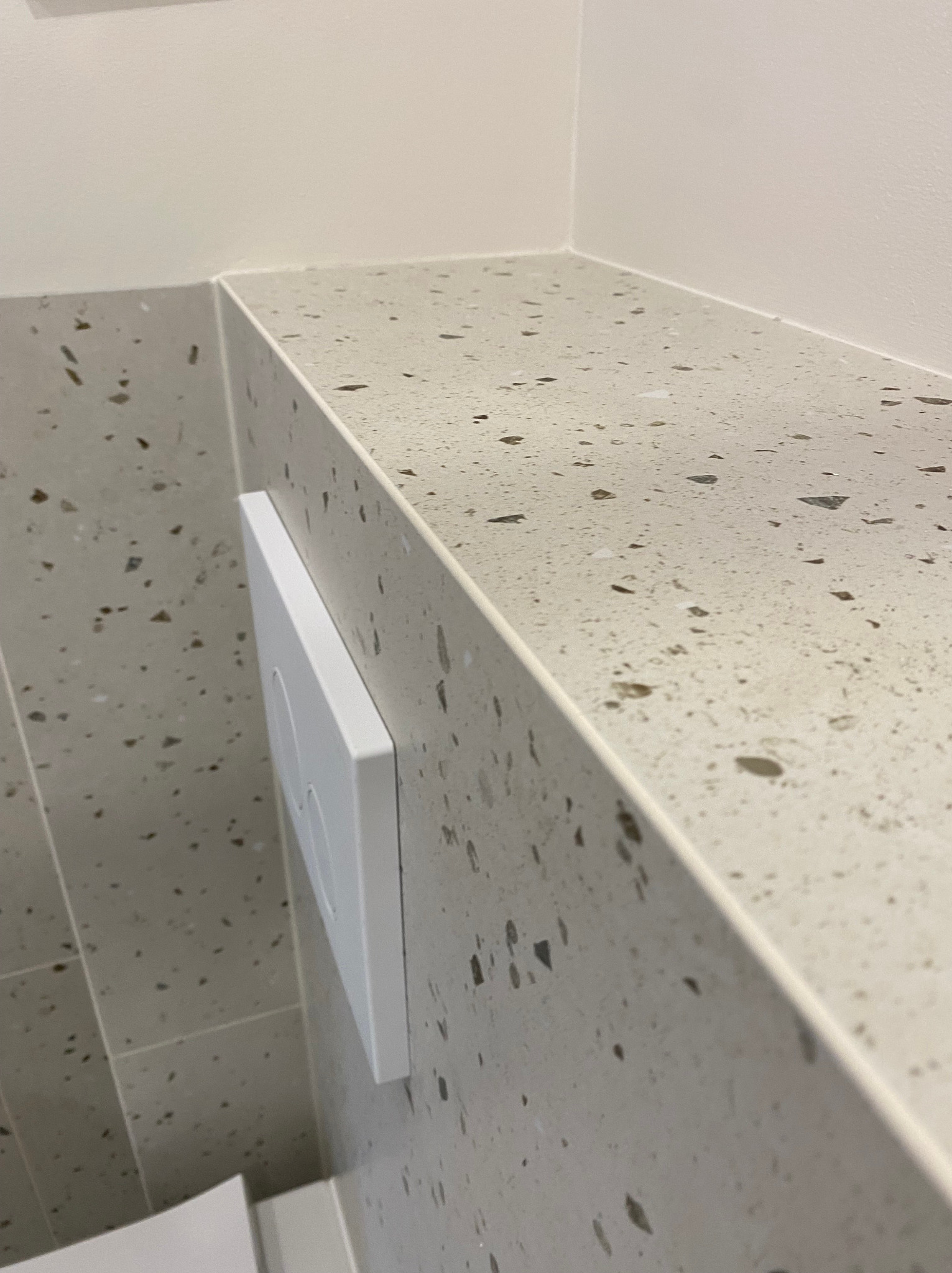 Detale wykończenia łazienki w Katowicach: zbliżenie na ścianę i półkę z płytek lastryko w odcieniach szarości, z widocznym przyciskiem spłuczki WC.