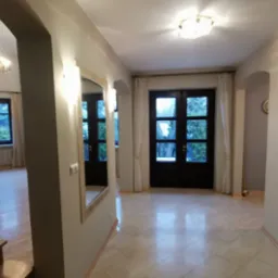 Jasny hol z drewnianymi schodami, marmurową podłogą, lustrem w ozdobnej ramie i oknami z widokiem na zieleń.