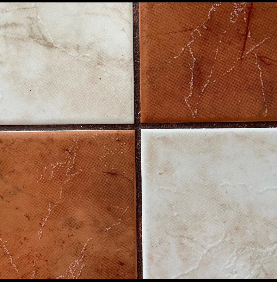 Cztery kwadratowe płytki podłogowe w kolorach beżowym i rdzawym, ułożone w szachownicę, z widocznymi smugami imitującymi marmur.