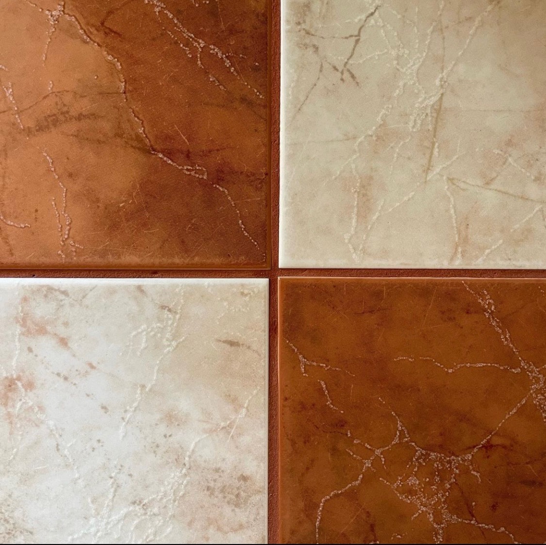 Cztery kwadratowe płytki podłogowe: dwie brązowe z marmurkowym wzorem i dwie beżowe z jasnymi żyłkami, ułożone naprzemiennie.