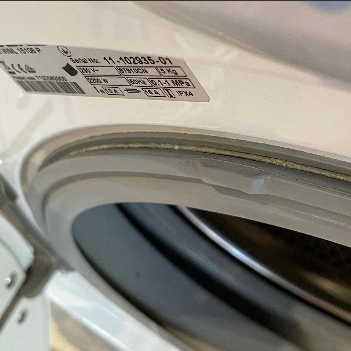 Uszczelka drzwi pralki z widocznymi zabrudzeniami i naklejką z numerem seryjnym.