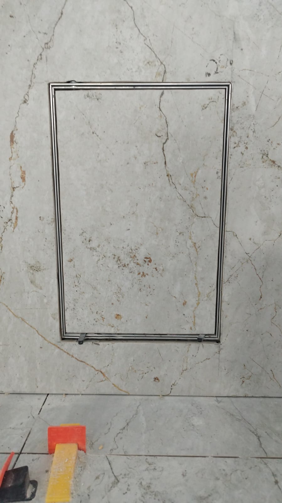 Ukryta rewizja w płytkach imitujących marmur, z widocznymi klinami poziomującymi.