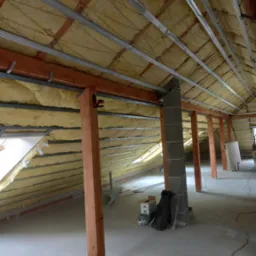 Poddasze w trakcie izolacji: widoczne drewniane słupy nośne, metalowy stelaż i wełna mineralna, przygotowane do dalszych prac wykończeniowych.