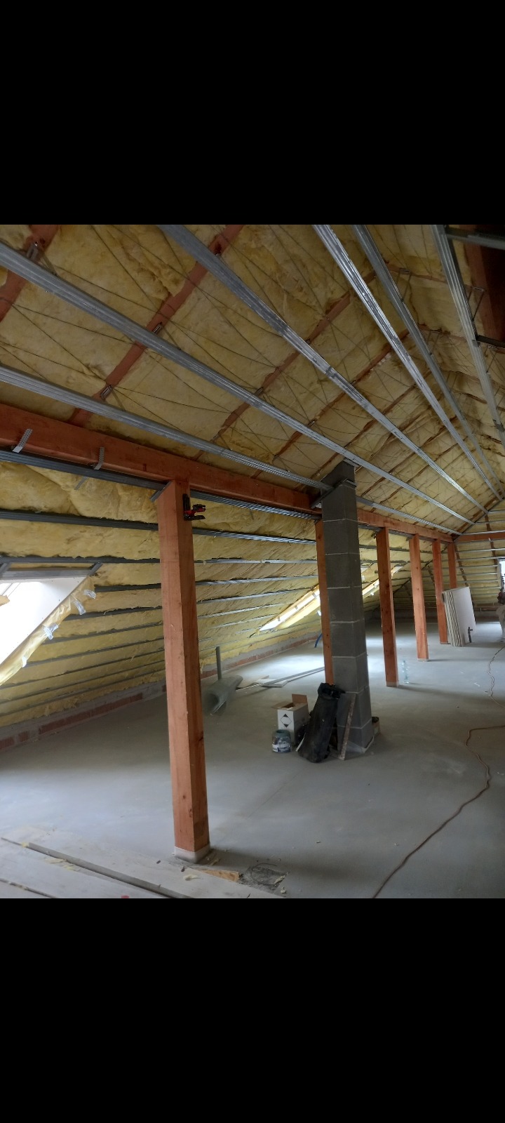 Poddasze w trakcie izolacji: widoczne drewniane słupy nośne, metalowy stelaż i wełna mineralna, przygotowane do dalszych prac wykończeniowych.