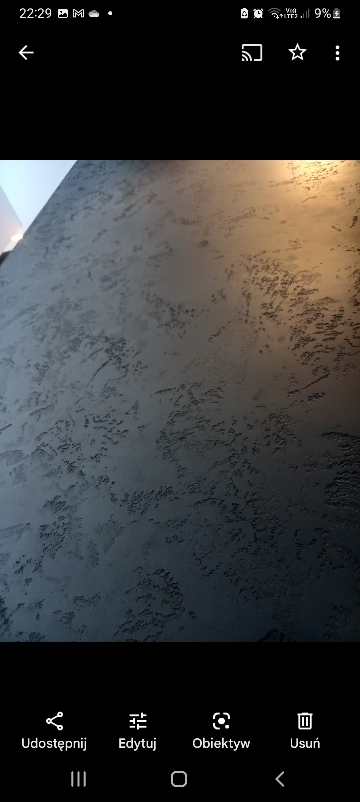 Szpachlowana ściana w Gorlicach z wyraźną fakturą w odcieniach szarości, oświetlona ciepłym światłem z góry, tworząca efekt trójwymiarowości.