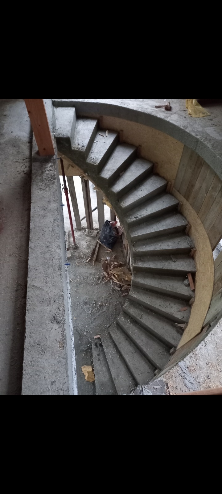 Betonowe schody spiralne w trakcie budowy, widoczne szalunki i podpory, surowy stan wykończenia, widok z góry.