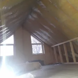 Poddasze domu z ocieplonym skośnym dachem wełną mineralną zabezpieczoną folią, widoczne okna dachowe i fragment drewnianej konstrukcji ścianki działowej.