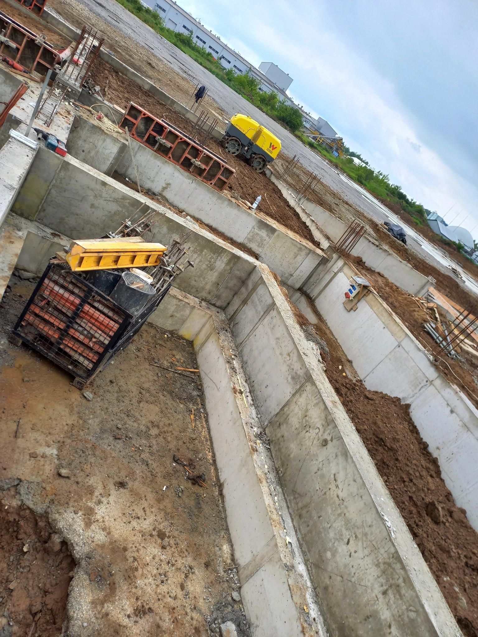 Budowa fundamentów w Iwkowej: Wykopane i zalane betonem rowy fundamentowe, widoczne zbrojenia i maszyna budowlana w tle, ziemia częściowo zasypana.