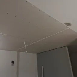 Sufit z płyt kartonowo-gipsowych, widoczne łączenia, wkręty, fragment instalacji elektrycznej i przygotowane miejsce na oświetlenie w nowym pomieszczeniu.