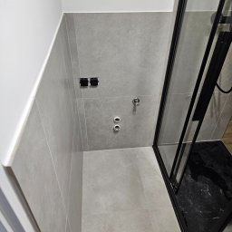 EUROBUD REMONTY WYKOŃCZENIOWE MYKOLA MUKIIENKO - Wykończona łazienka z szarymi płytkami, czarną kabiną prysznicową i przygotowanymi przyłączami wodno-kanalizacyjnymi oraz elektrycznymi.