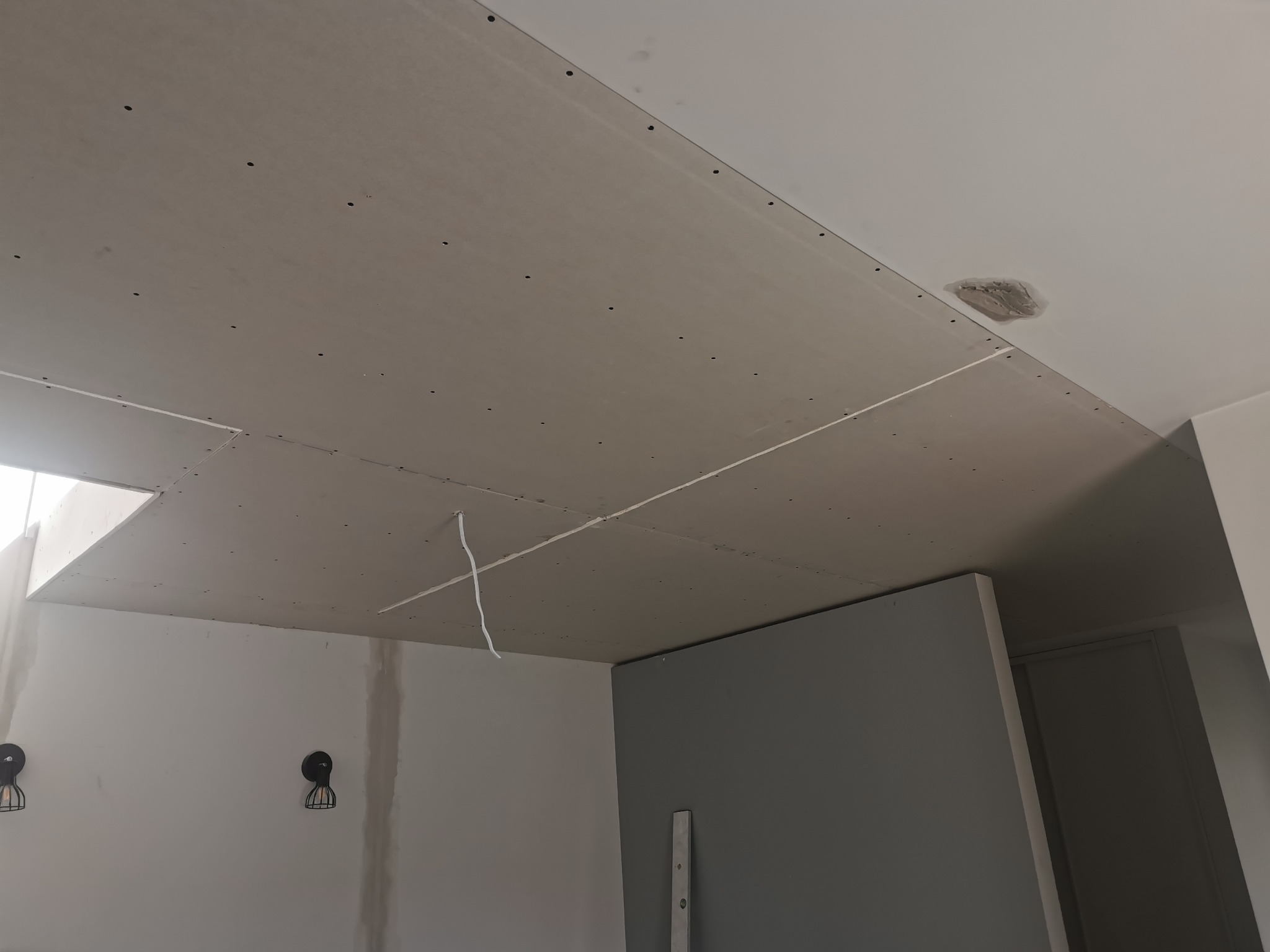 Sufit z płyt kartonowo-gipsowych, widoczne łączenia, wkręty, fragment instalacji elektrycznej i przygotowane miejsce na oświetlenie w nowym pomieszczeniu.